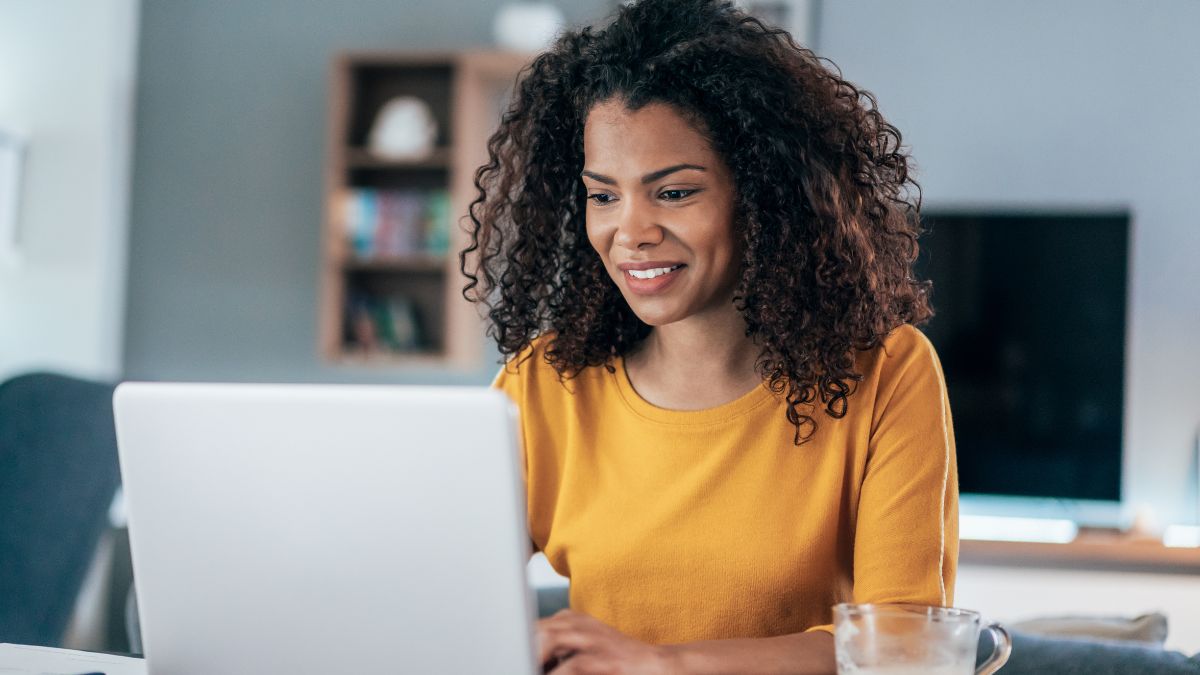 Uma mulher negra com uma camisa amarela trabalhando em home office em seu laptop