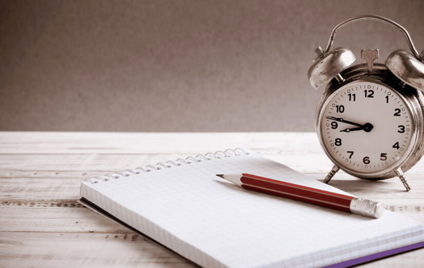 Um caderno com uma caneta e um despertador