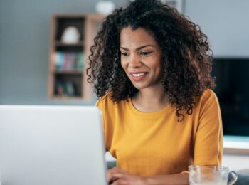 Uma mulher negra com uma camisa amarela trabalhando em home office em seu laptop